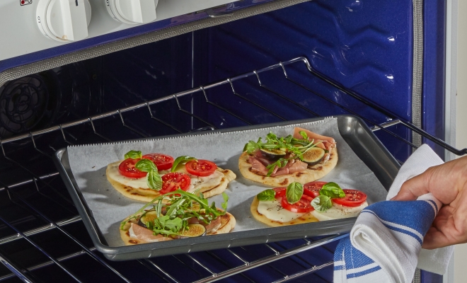 Person removing a baking sheet from the oven lined with parchment paper and personal pizzas 