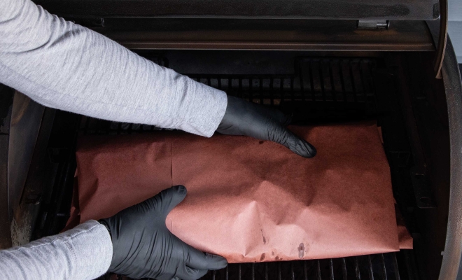 A person adding meat wrapper on pink paper to the grill