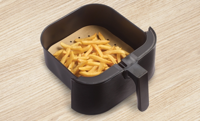 Cooked french fries sitting on top of an air fryer liner in an air fryer basket